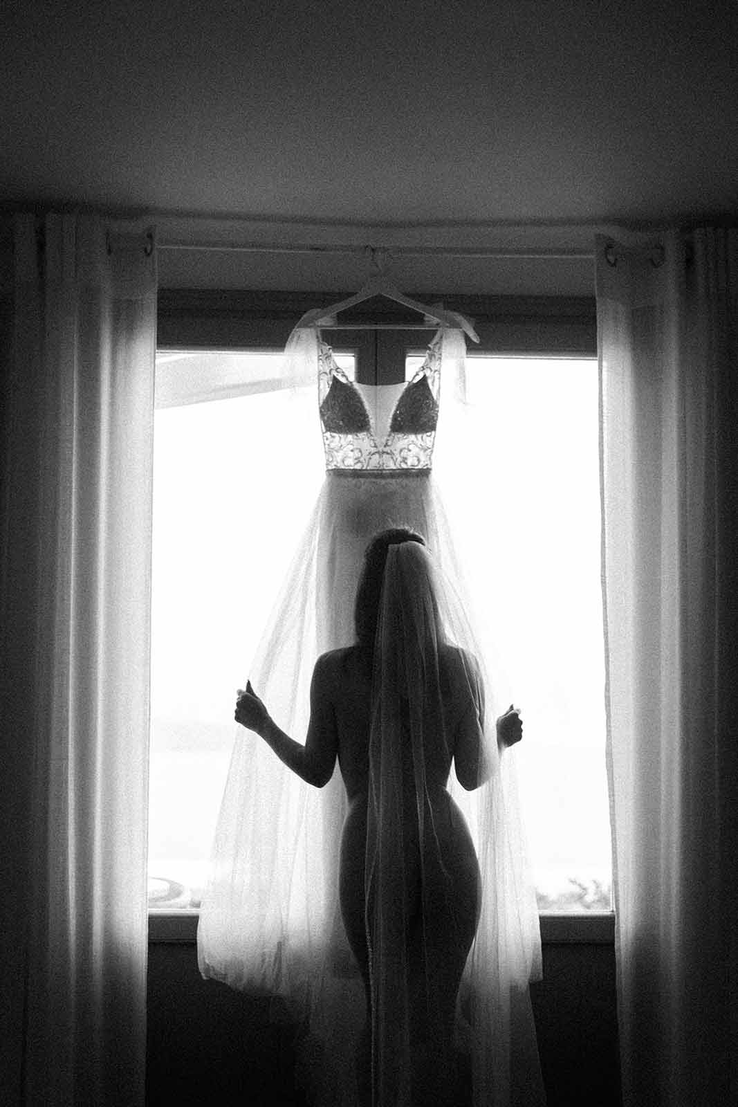 getting ready in Potsdam mit Braut stehend vor dem Fenster und ihrem Hochzeitskleid Schwarz Weiß.