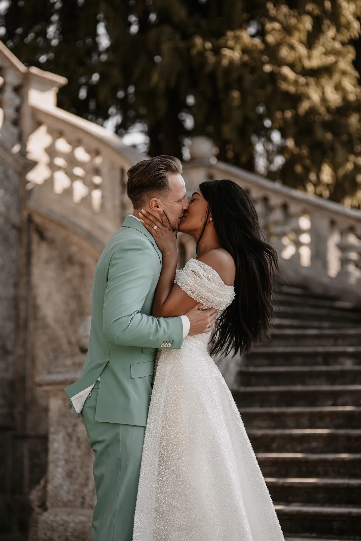 Ein Hochzeitspaar küsst sich auf einer Steintreppe