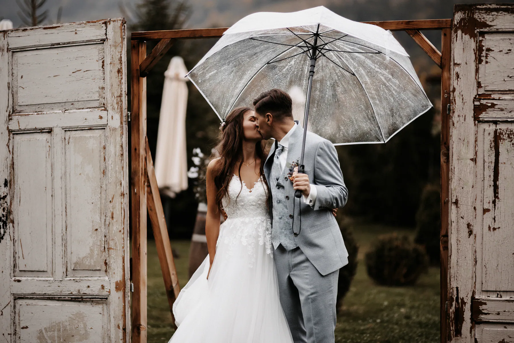 Ein Hochzeitspaar küsst sich im Regen unter einem durchsichtigen Schirm
