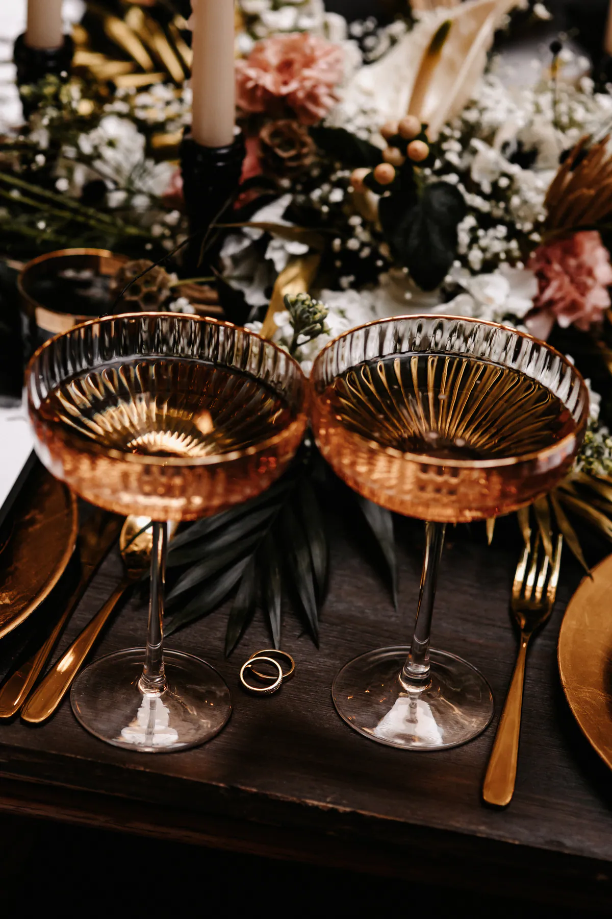 Zwei gefüllte Champagnerschalen stehen zwischen Kerzen und Blumen