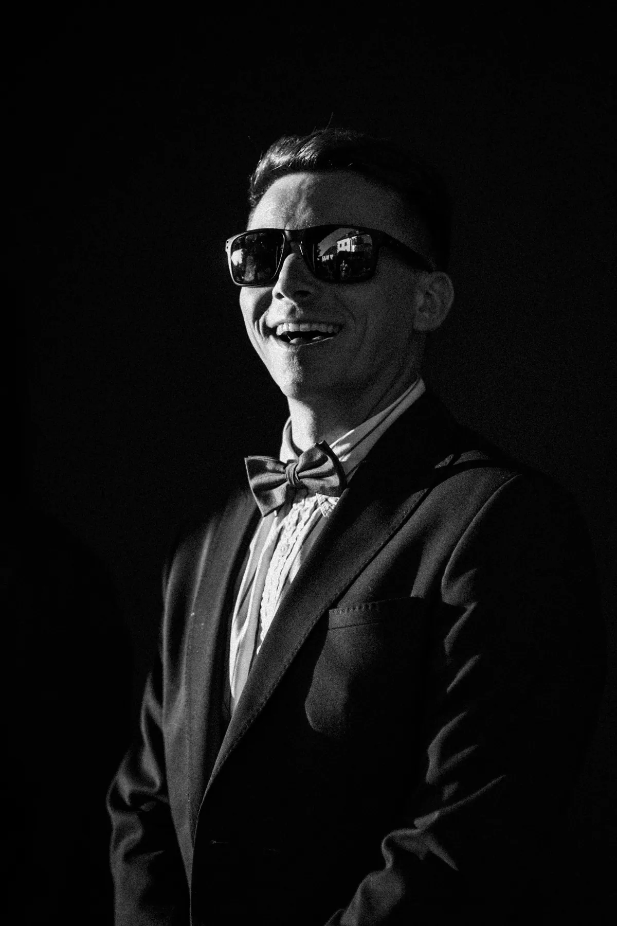 Ein Hochzeitsgast mit Sonnenbrille lacht im harten Seitenlicht