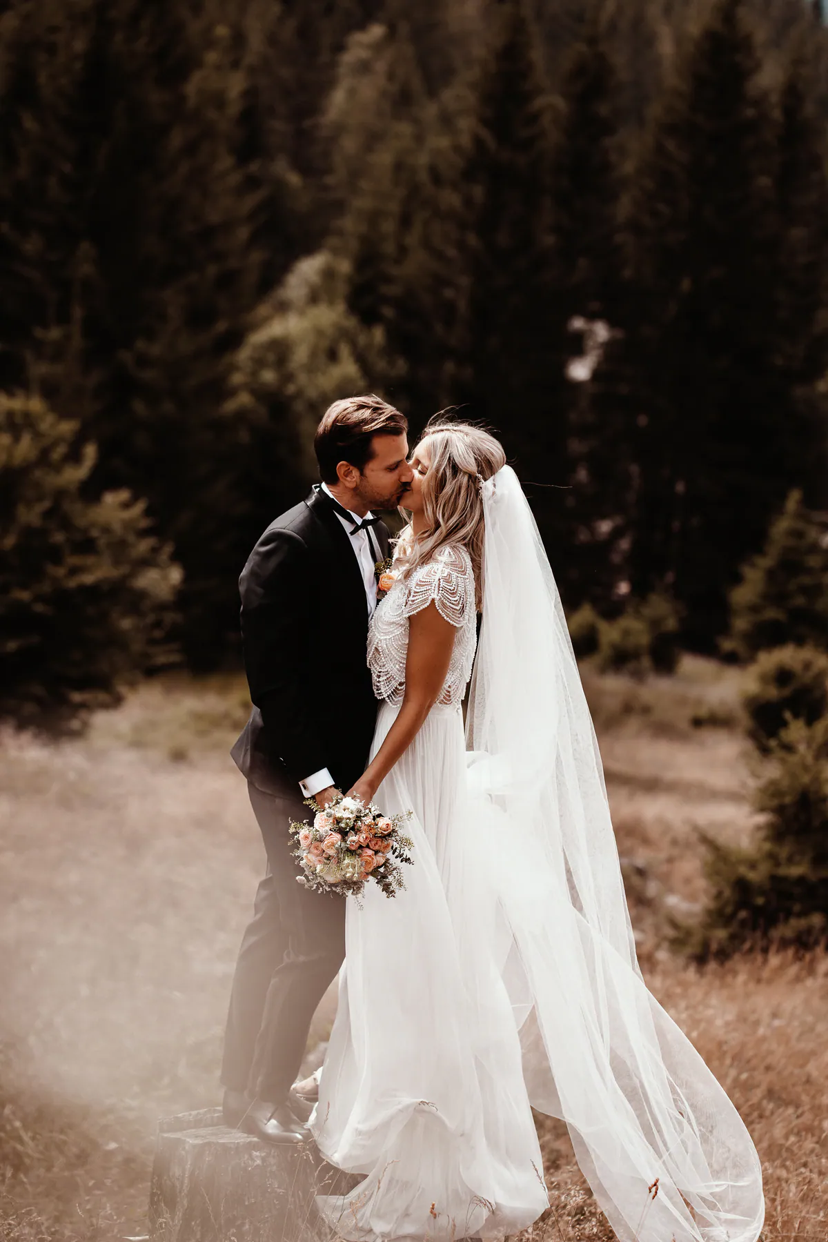 Ein Hochzeitspaar küsst sich zwischen hohen Bäumen