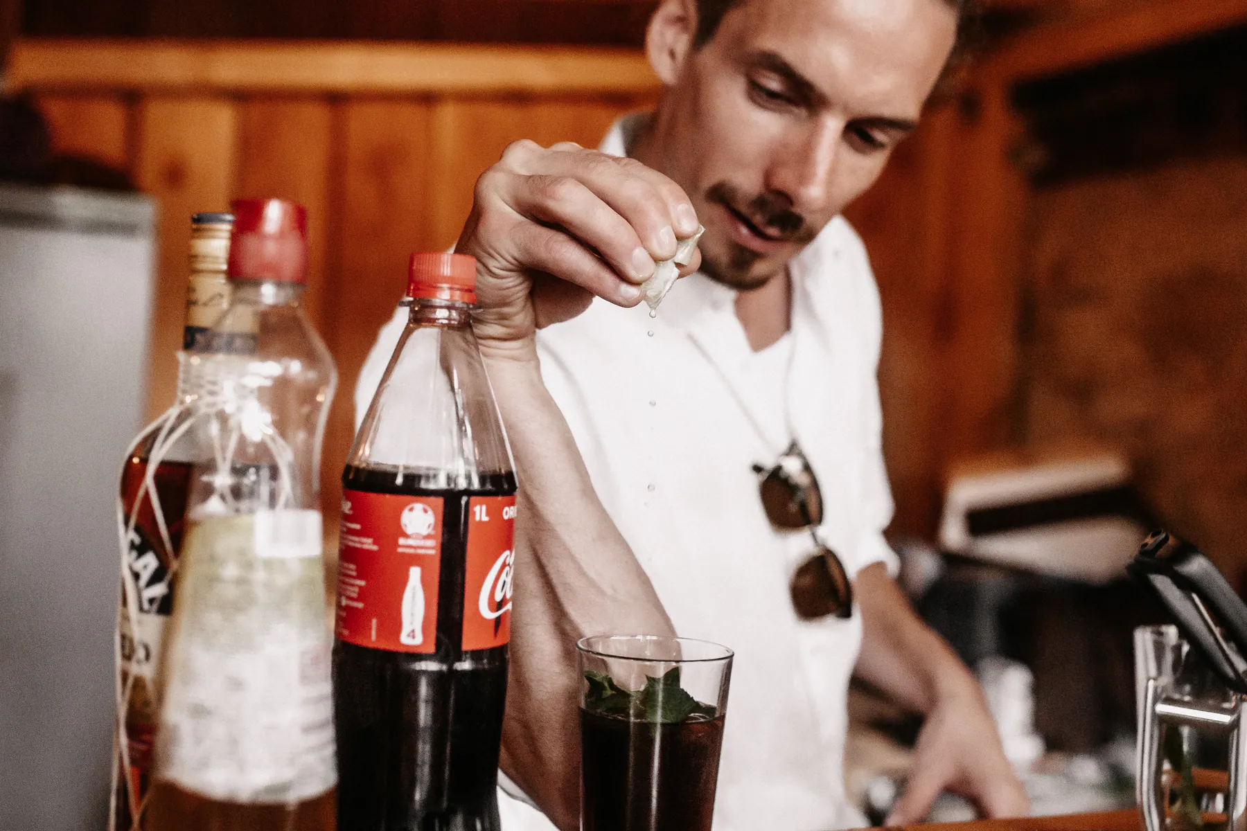 Ein Gast presst hinter einer Holzbar eine Limette über ein Glas mit Minze