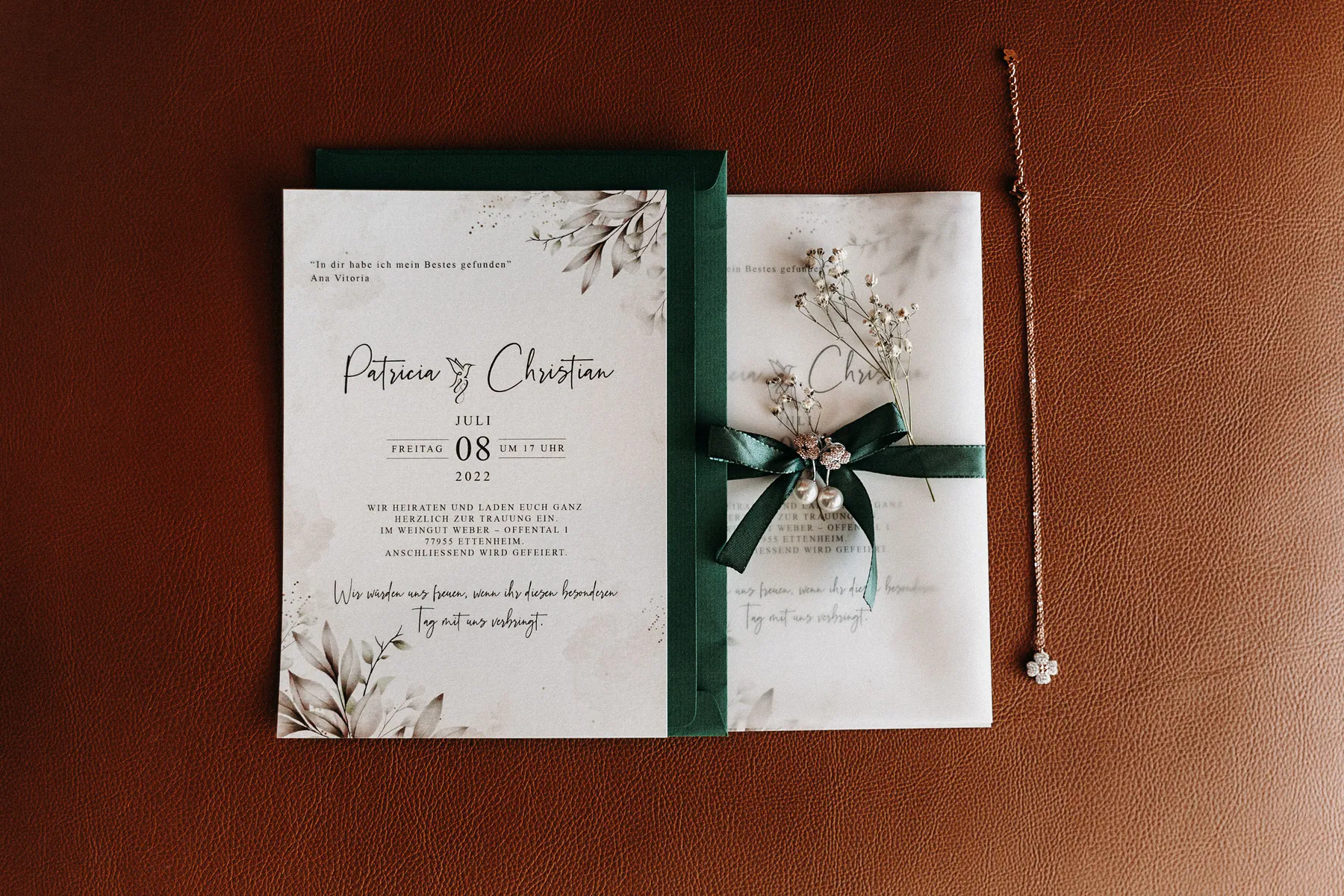 Hochzeitseinladung, Schmuck und Trockenblumen liegen auf braunem Leder