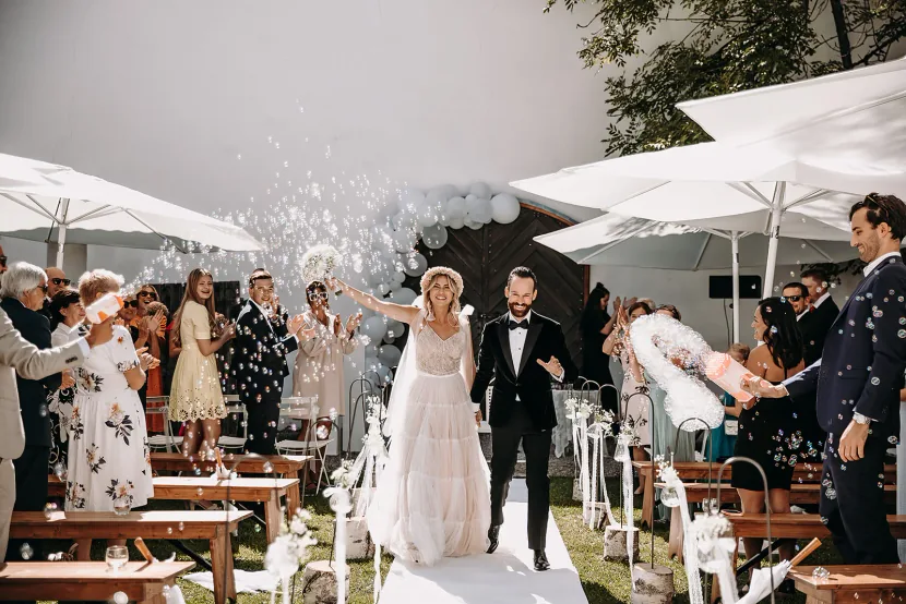 Ein Hochzeitspaar geht lachend durch ein Spalier aus Seifenblasen