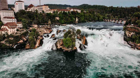 Breiter Blick auf den Rheinfall mit Felsen und Gebäuden am Ufer