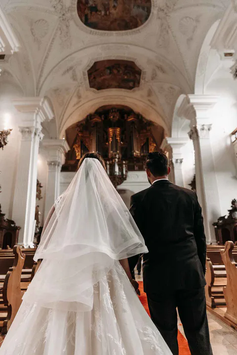 Braut und Mann gehen von hinten gesehen durch ein reich verziertes Kirchenschiff