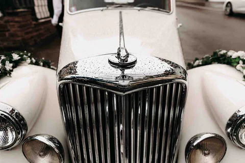Front eines weißen Oldtimers mit Kühlergrill und Kühlerfigur
